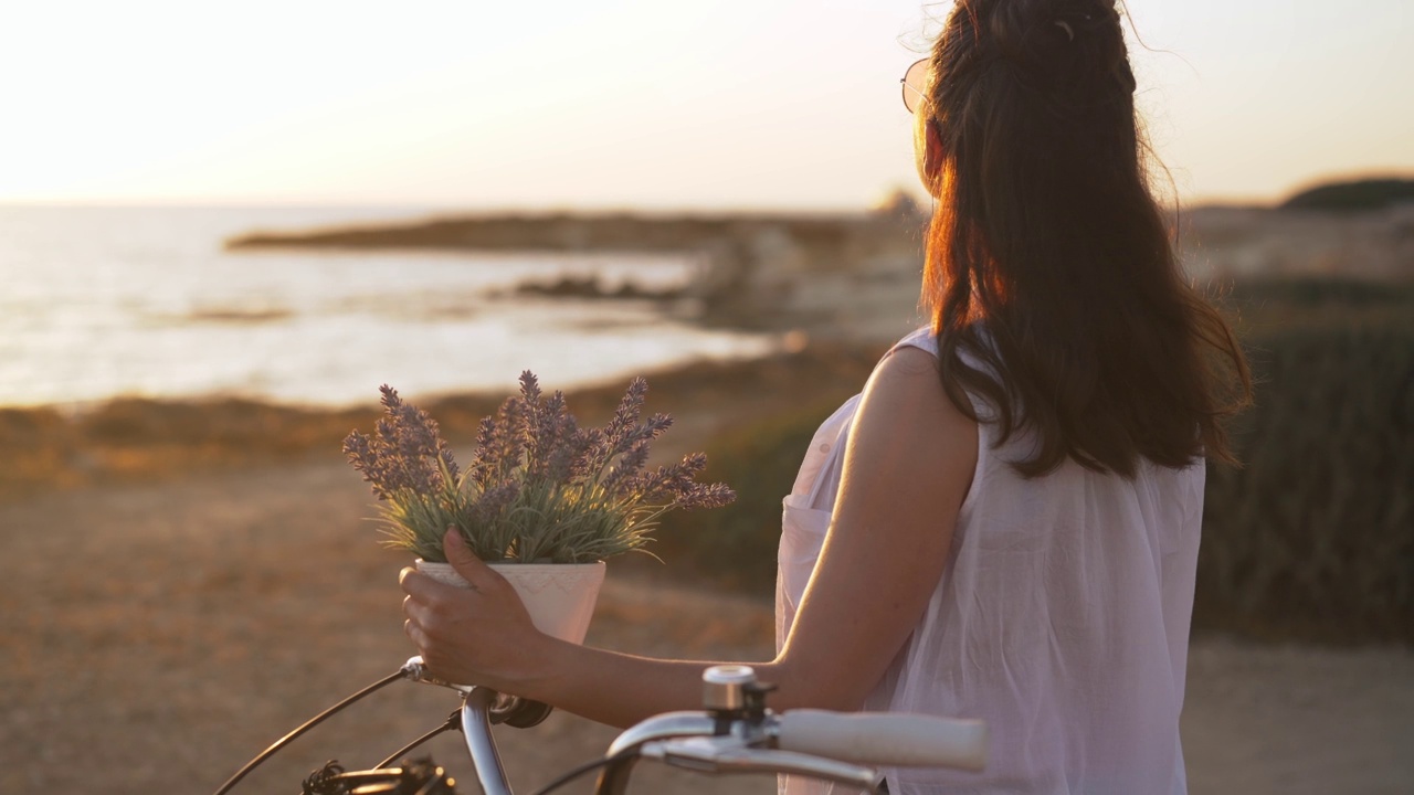 年轻、冷静、自信的女子站在地中海海滩上，手持鲜花欣赏夕阳。中景拍摄了愉快放松的高加索游客在塞浦路斯度假。视频素材