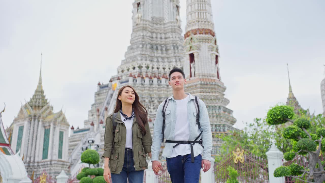 亚洲年轻夫妇在城市旅行蜜月旅行的肖像。新婚男女背包客一起在泰国度假，互相抱着胳膊看相机。视频素材