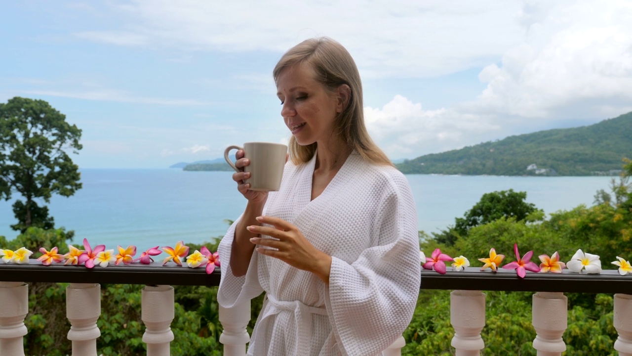 穿着酒店浴袍的女人在海景露台上喝着早上的热咖啡视频素材