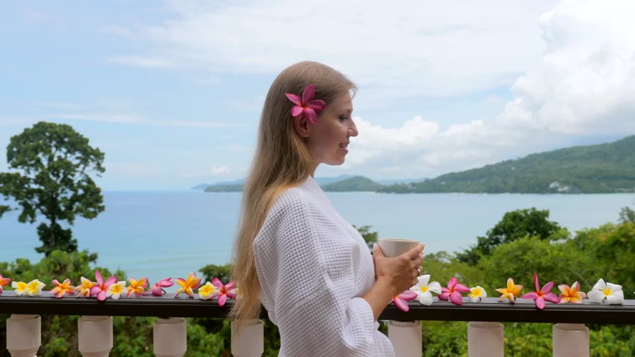 迷人的年轻女子与一杯热的早晨咖啡在白色的酒店浴袍视频素材