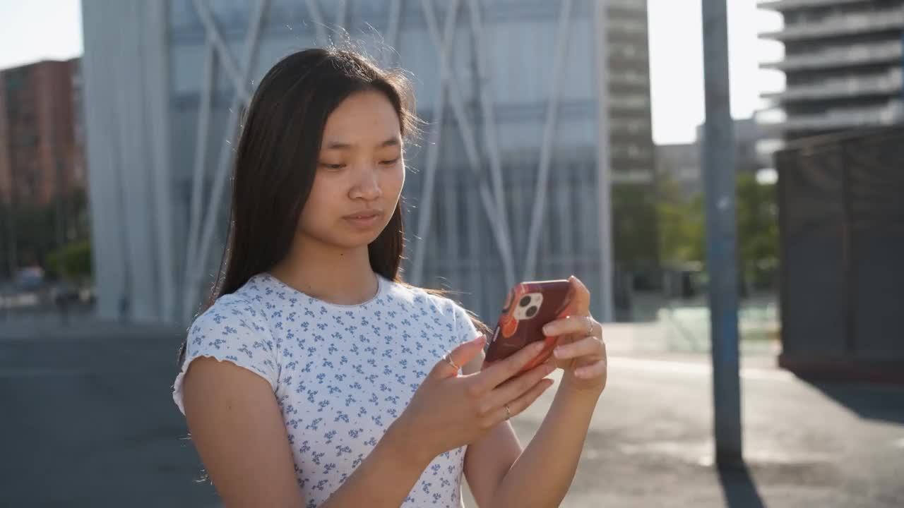 微笑的年轻女子站在户外的街道上用手机。视频素材