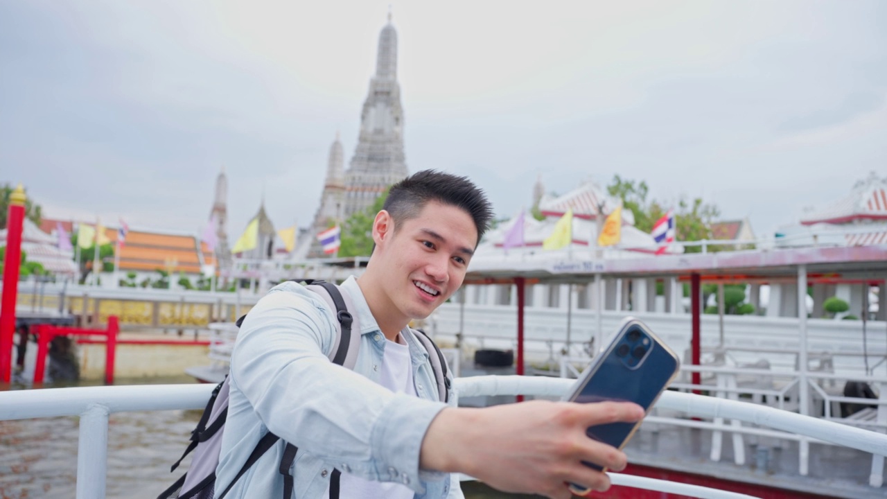 一名亚洲男子背包客用手机拍摄佛寺。年轻的男性游客独自在城市的街道上旅行，用手机记录视频日志在泰国度假旅行。视频素材