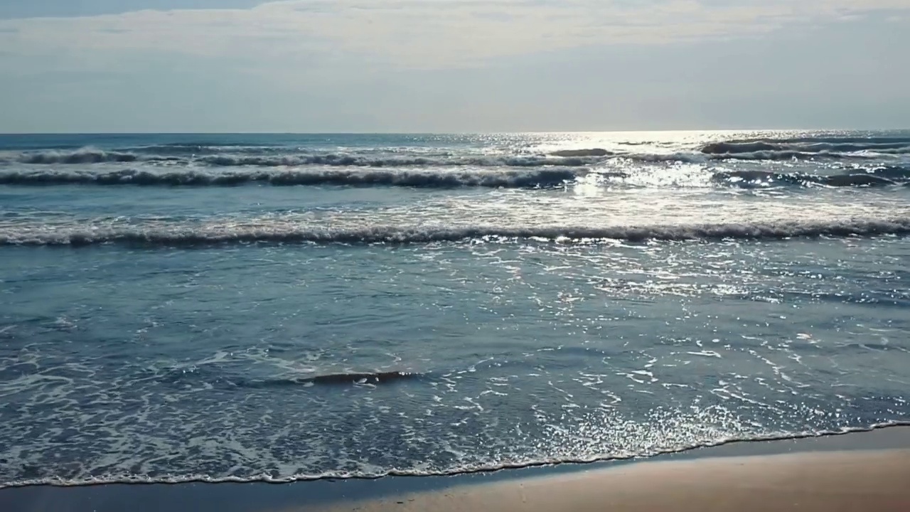 白天看海景。海浪涌向海岸。海浪冲刷着沙滩。阳光在海水中闪闪发光。视频素材