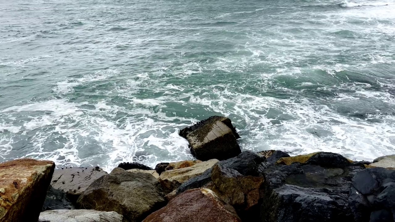 当海浪撞击岩石岬时产生了湍流，在蓝绿色的背景下形成了泡沫。视频素材