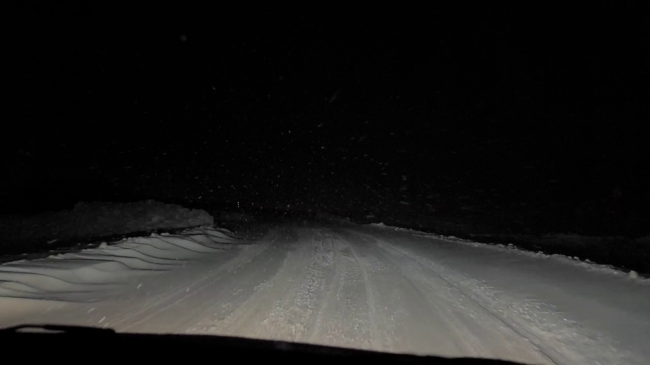 一辆汽车在大雪纷飞的夜晚行驶在路上。透过汽车挡风玻璃看。严重的暴风雪视频素材