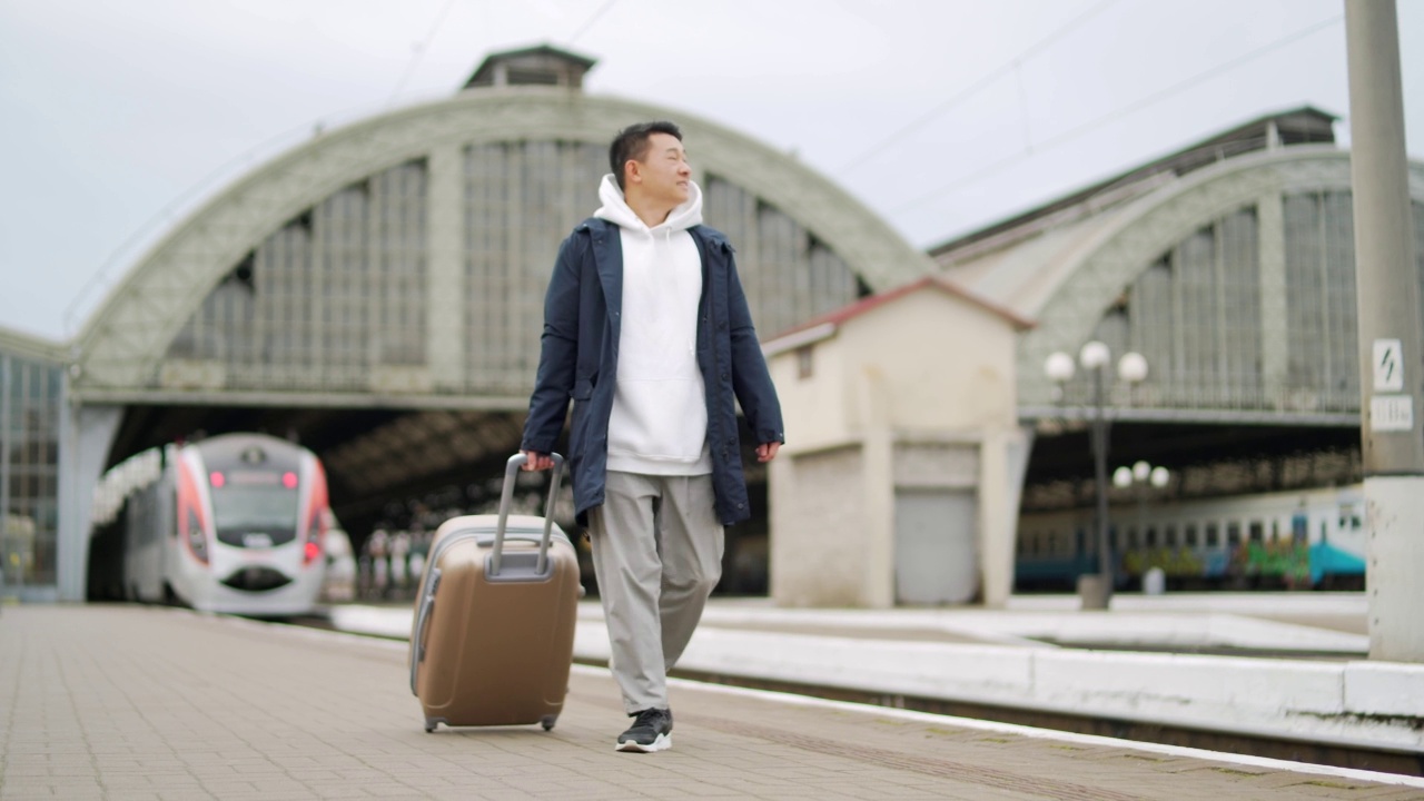 男亚洲旅客乘火车到达或离开家乡在镇上，带着大旅行箱，旅客在火车站火车站男旅行者走在站台上视频素材