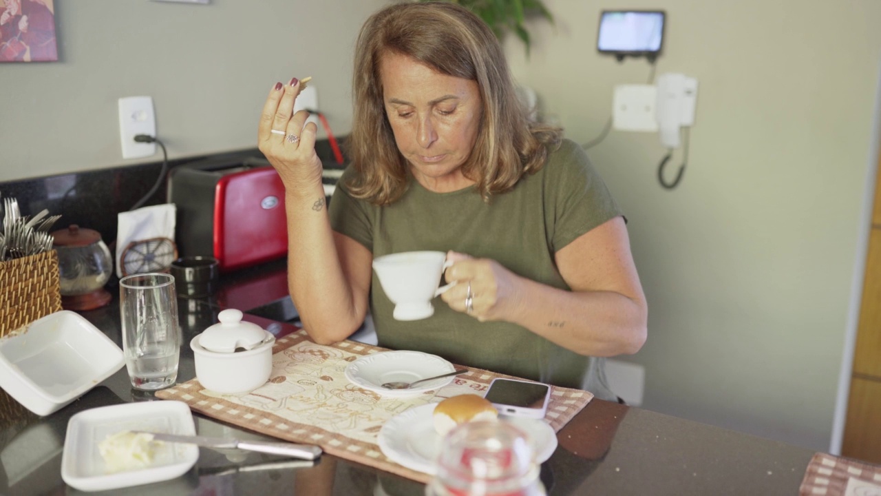 成熟的女人在厨房吃早餐的时候查看她视频素材