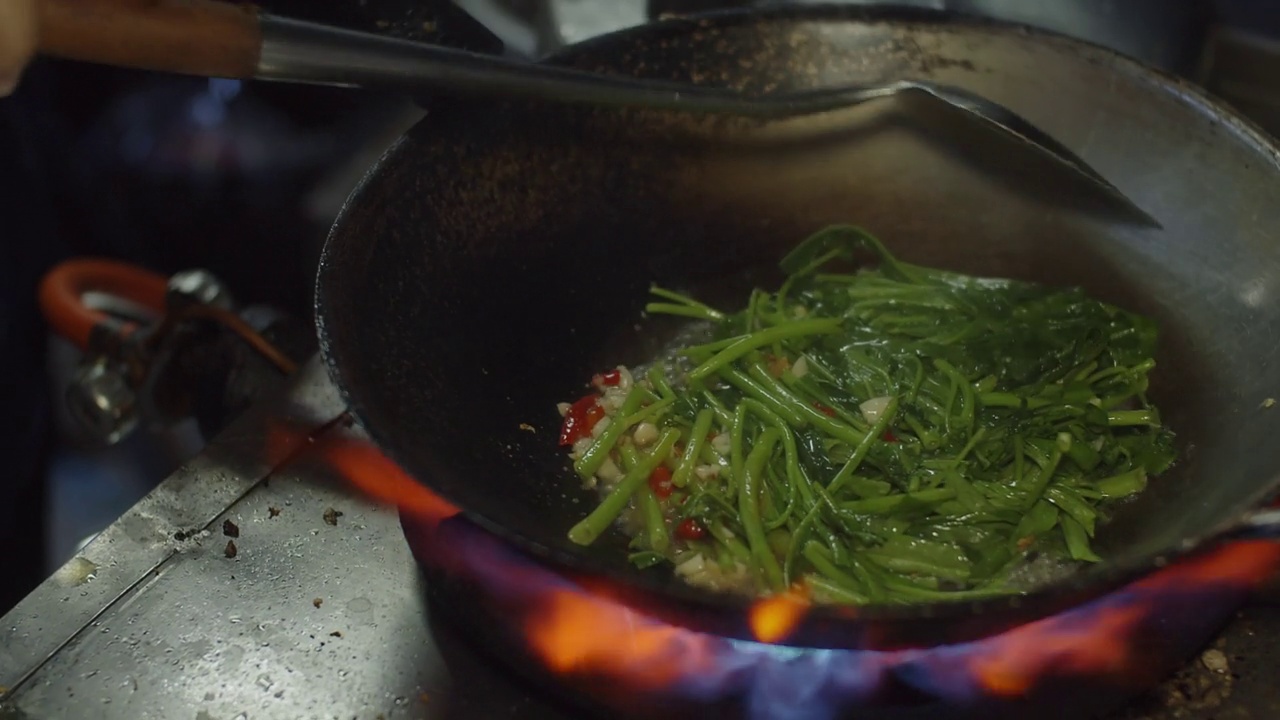 图为厨房里用火煎锅炒的中国牵牛花或菠菜，亚洲泰式食物，泰国流行的街头小吃菜单视频素材