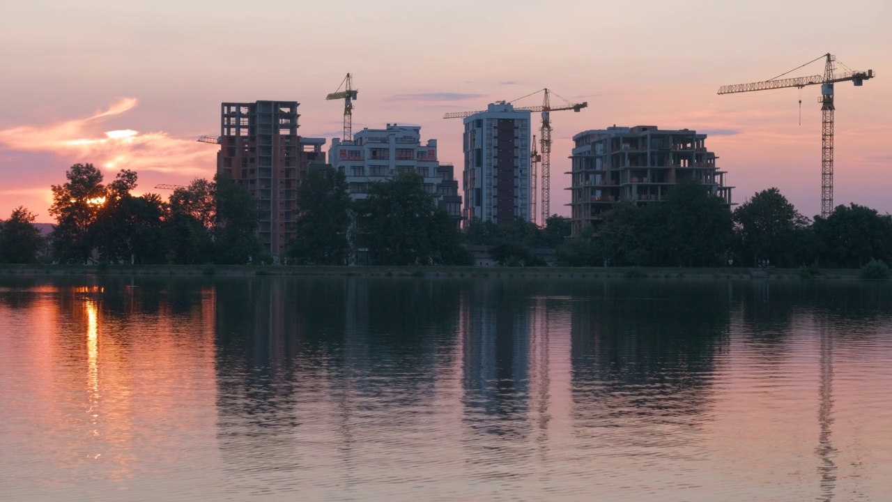 湖滨景观，建筑建筑的黑色剪影反映在湖水和远处步行的行人在明亮的日落堤上视频素材