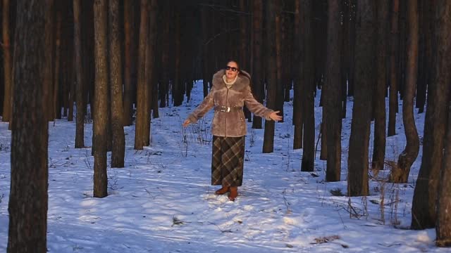 美丽的女人在冬天的森林穿着毛皮大衣和太阳镜。它正在下雪。她在冬天很快乐。面带微笑。缓慢的运动。冬天的公园。冬季森林。视频素材