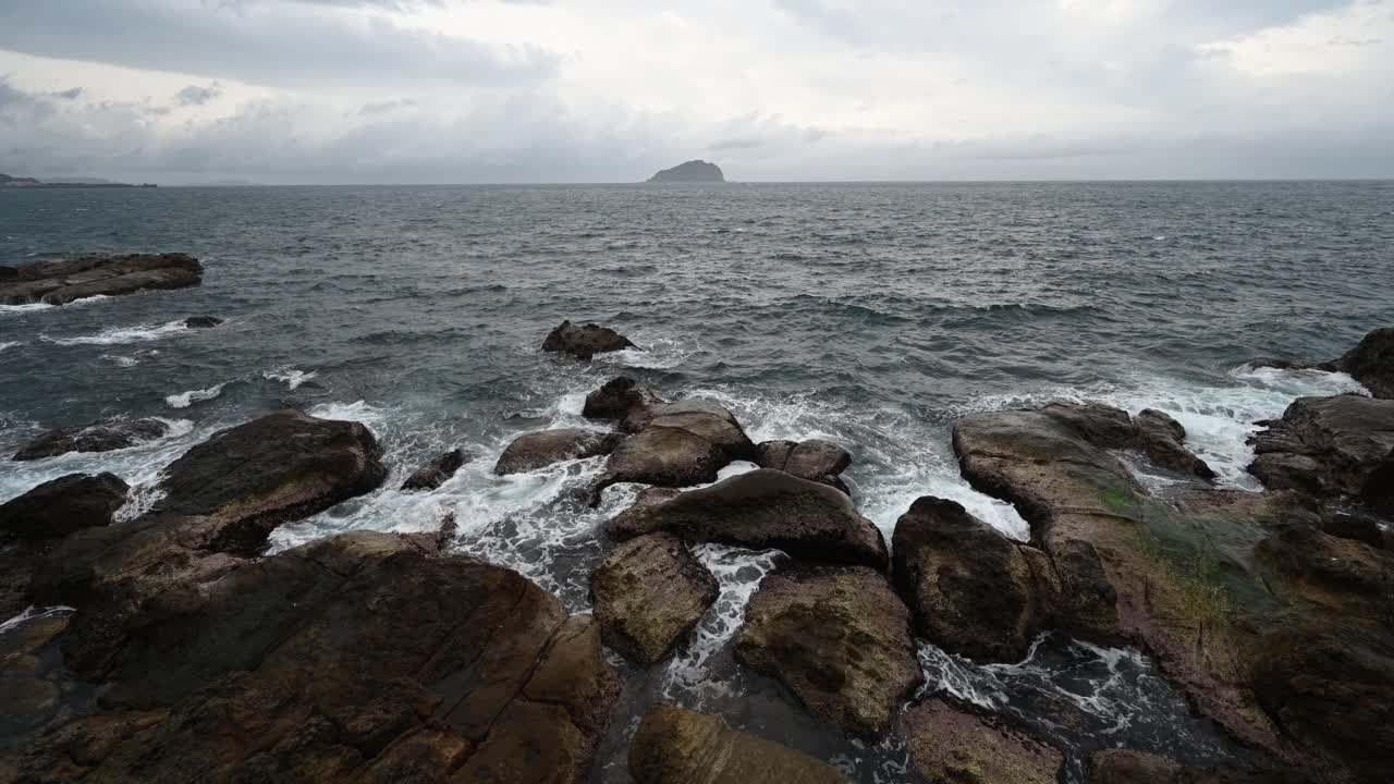 大风天附近的海岸线，大浪溅在岩石上，天空非常多云，和一个小岛在海洋中间，在台湾基隆市。视频素材