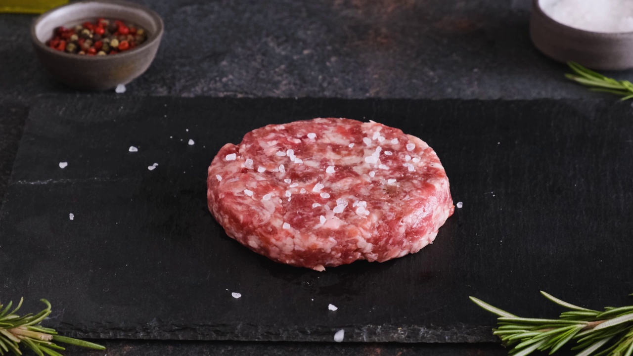 在黑色背景上腌制生牛肉汉堡肉饼。烹饪概念视频素材