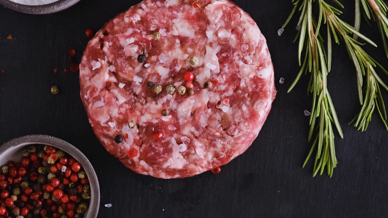 在黑色背景上腌制生牛肉汉堡肉饼。前视图。烹饪食物的概念视频素材