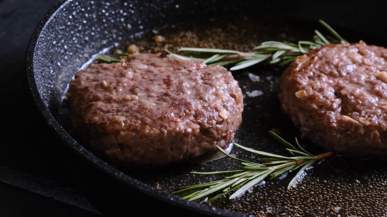 厨师手把迷迭香放入煎锅中与牛肉饼一起煎。烹饪食物的概念视频素材