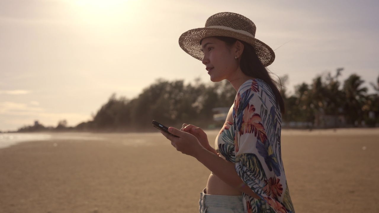 亚洲女性在日落时分的海滩上玩智能手机。视频素材