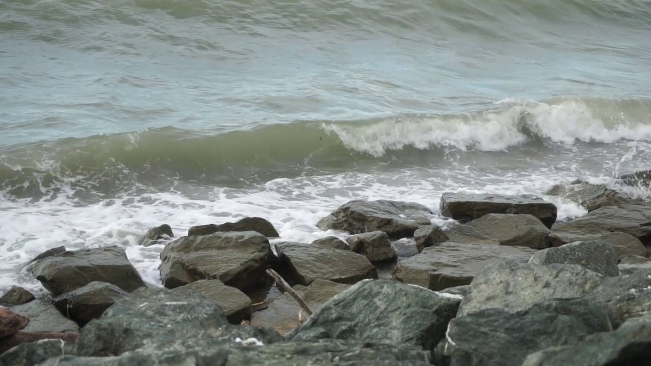 海浪冲击着多石的海岸。海浪拍打着岸边的石头，溅起水花。视频素材