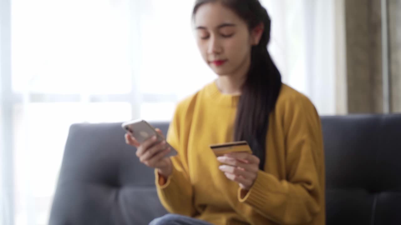 年轻的亚洲女性用信用卡在手机上购物，女性手持信用卡在网上购物。使用数码设备轻松支付。视频素材