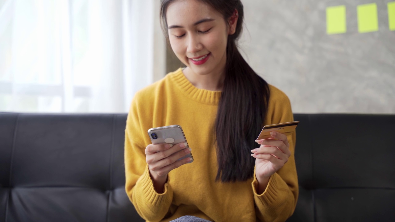 年轻的亚洲女性用信用卡在手机上购物，女性手持信用卡在网上购物。使用数码设备轻松支付。视频素材