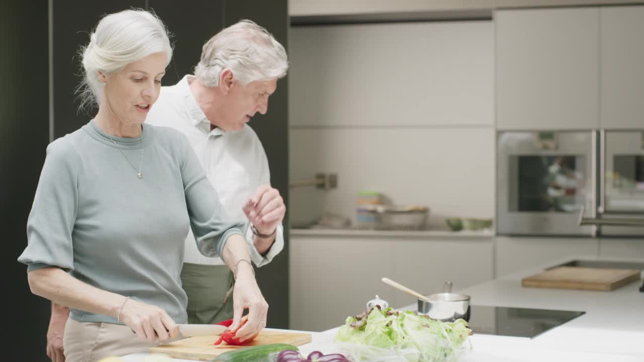 一对老年夫妇在家里的厨房做饭。一个成熟的男人和女人一起做健康的饭，享受放松，退休视频素材