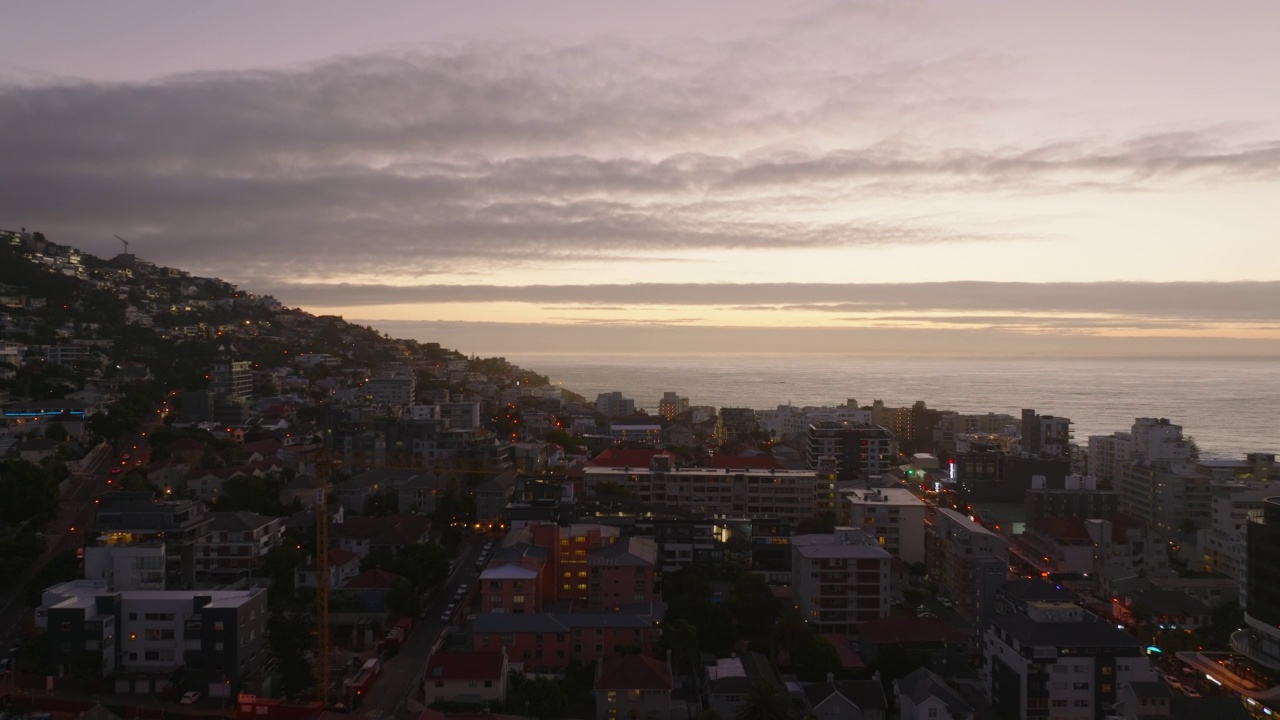 黄昏时分，在沿海城区上空向前飞行。鸟瞰图，在彩色的夕阳天空与云彩。开普敦，南非视频素材