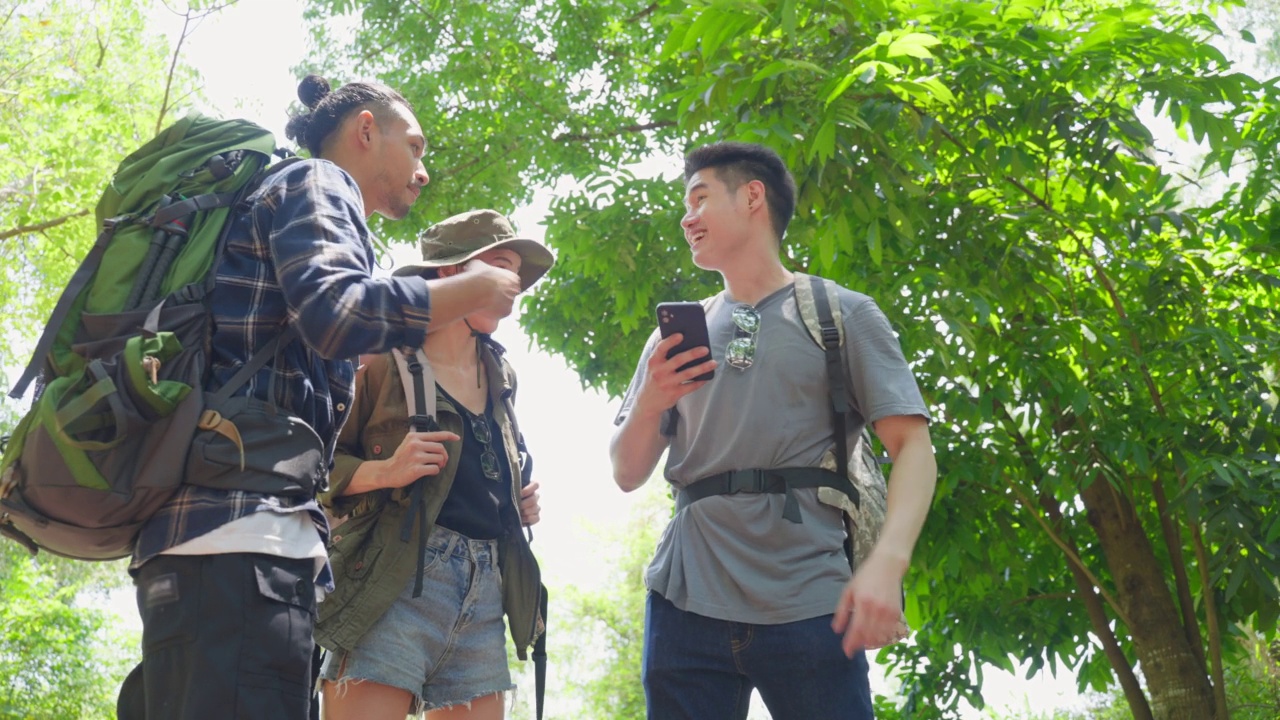 一群亚洲背包客在森林里玩得很开心。迷人的男人和女人朋友走和看地图在手机上找到方向在暑假假期旅行视频素材