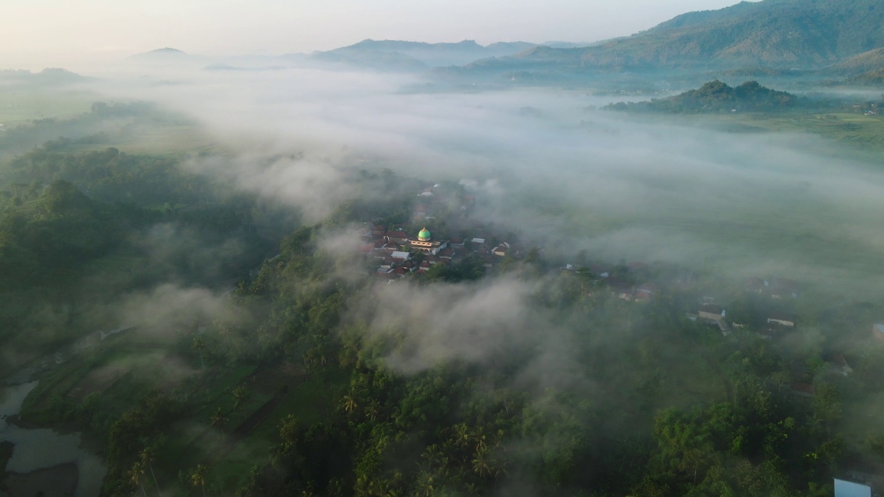 鸟瞰图，一个村庄的稻田和山丘在清晨笼罩在薄雾中视频素材