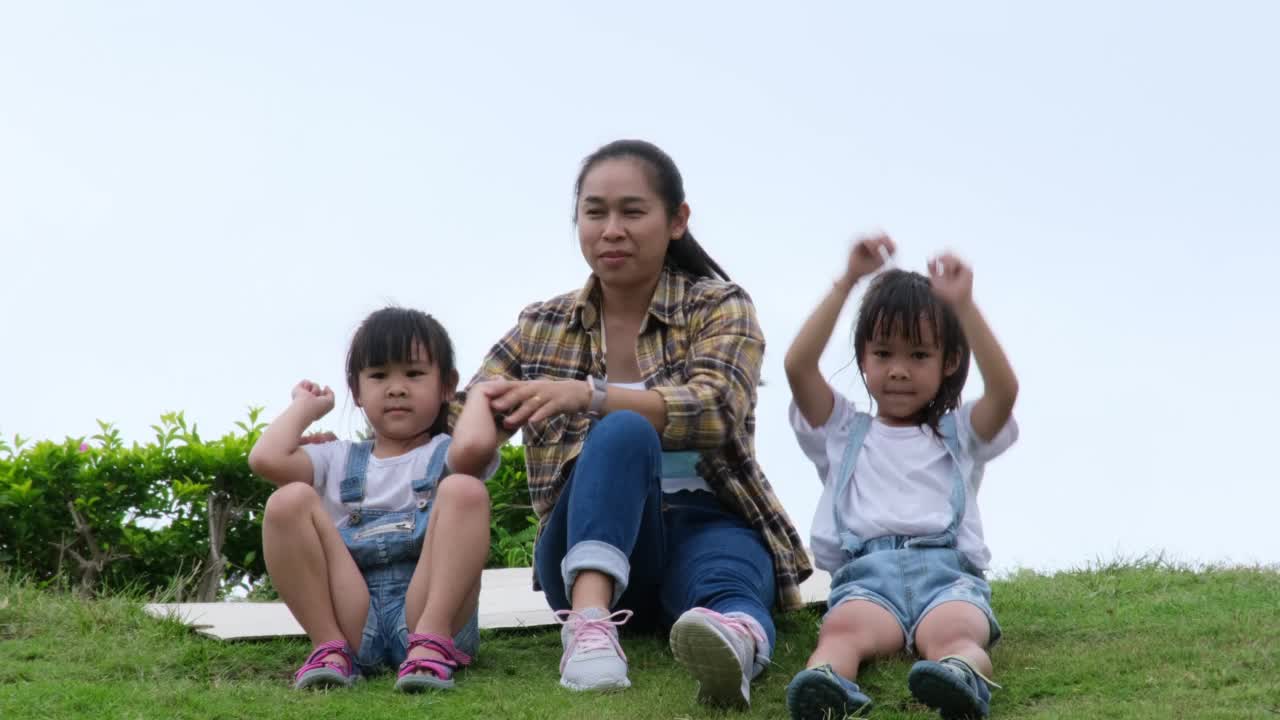 幸福的家庭，母亲和女儿坐在花园的小山上，在天空的背景下举起她的手臂，感觉自由。幸福快乐的概念。视频素材