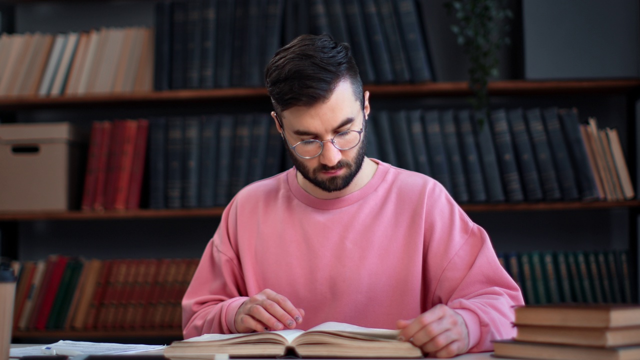 自信聪明的西班牙裔男子阅读纸质书在公共图书馆的书桌上翻页视频素材