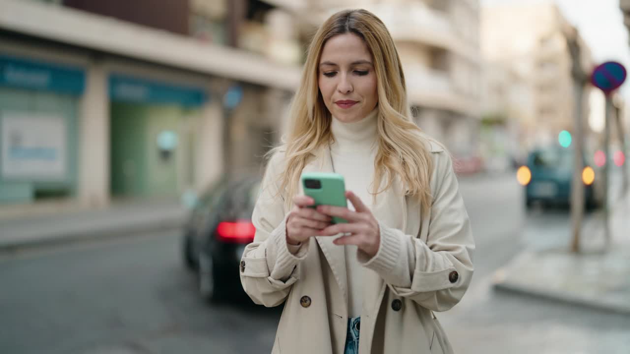 年轻的金发女子微笑着自信地在街上用智能手机自拍视频素材