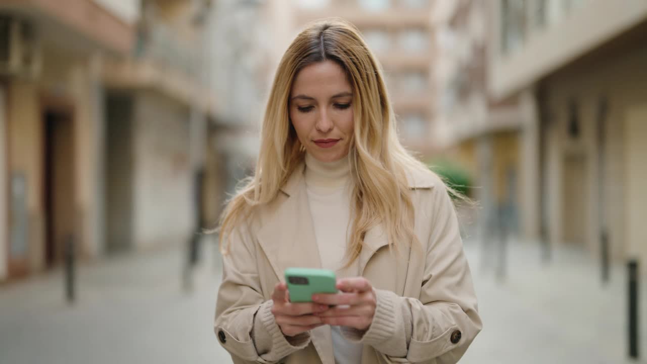 年轻的金发女子在街上用智能手机视频素材