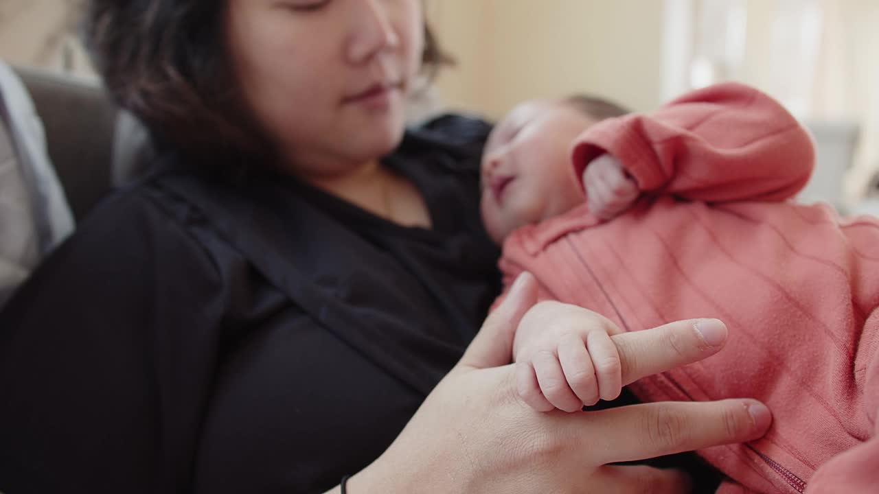 特写亚洲新生婴儿婴儿的手握住妈妈的手指，躺在妈妈的胳膊上，母爱亲情视频素材