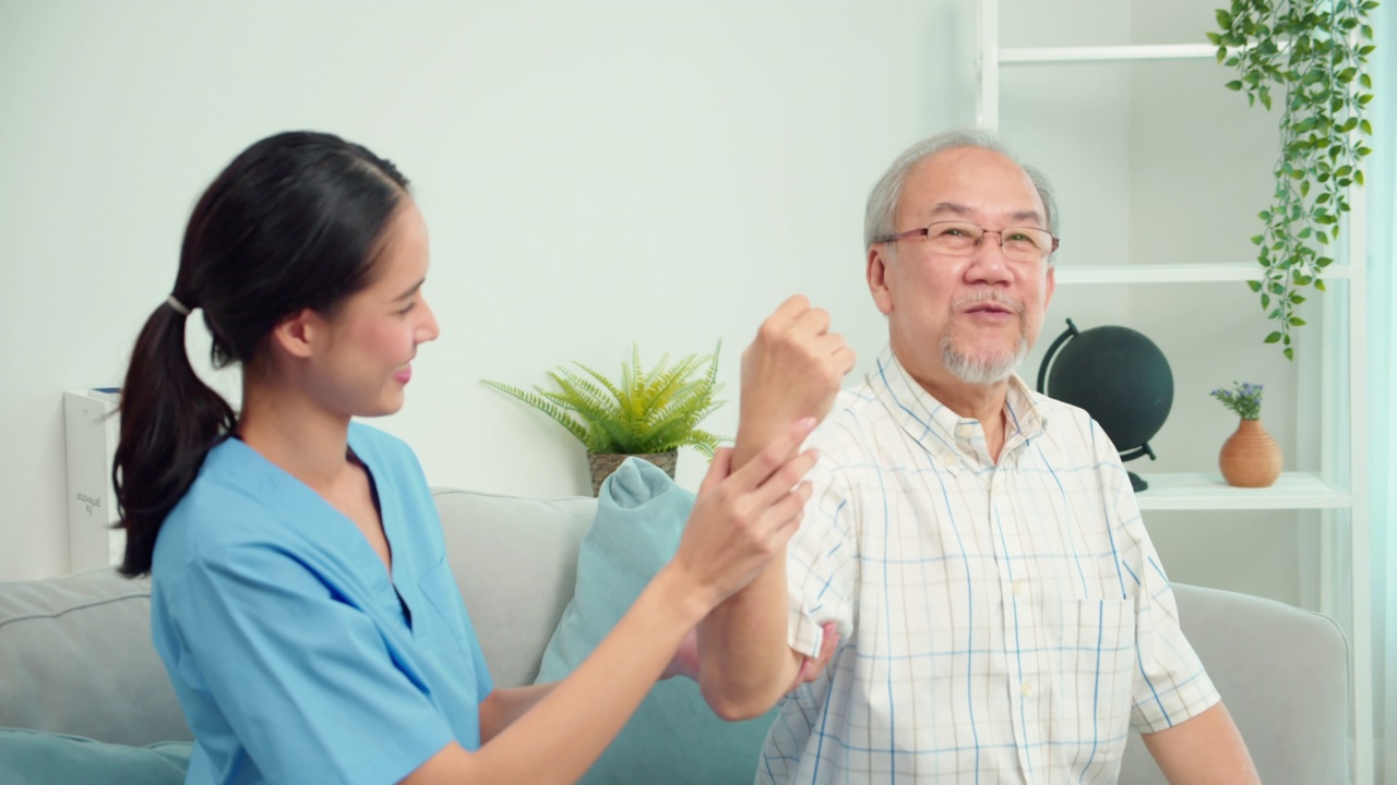 亚洲女性物理治疗师检查老年男性患者的手臂运动。护士在家中客厅沙发上协助对老年男性患者手臂进行物理治疗。视频素材