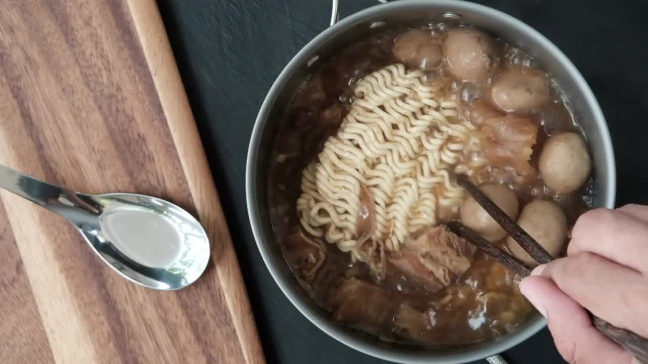 一个人在肉丸汤中煮方便面，牛肉汤沸腾，蒸汽喷涌而出。照片，俯视图，慢动作。视频素材