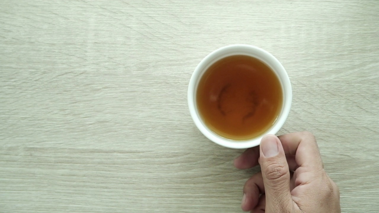 一个男人的手正在浅棕色的木桌上用白色的茶杯泡茶。俯视图，慢动作视频素材