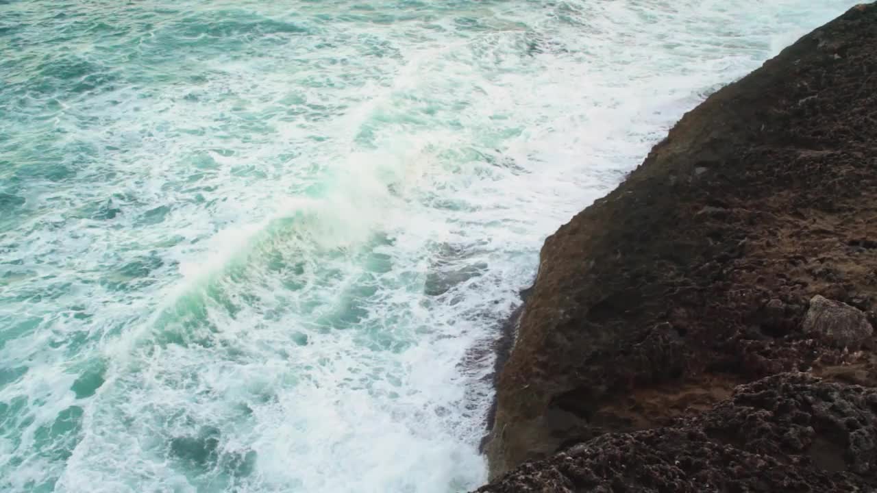 大海撞击岩石海岸，绿色的水飞溅和创造白色泡沫，从上面观看，慢动作视频视频素材