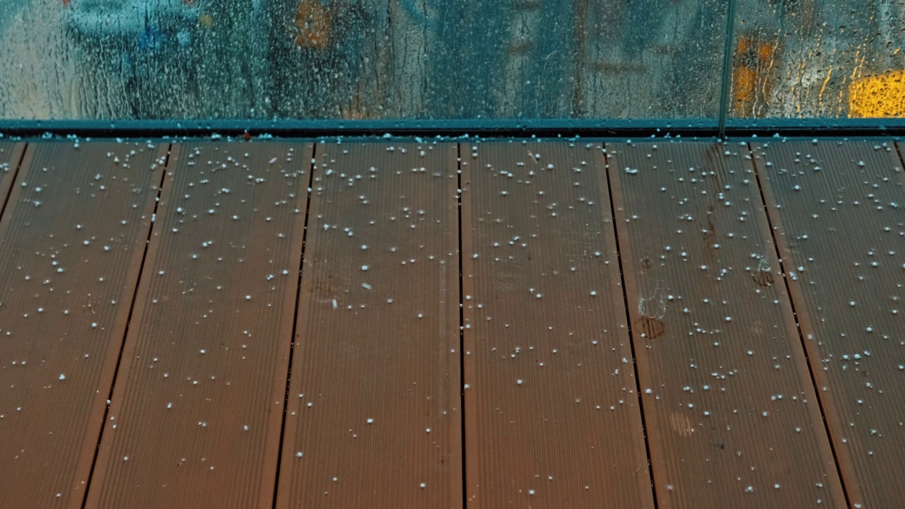 在暴风雨季节，雨滴顺着窗户流下，冰雹击中阳台上的复合木板视频素材