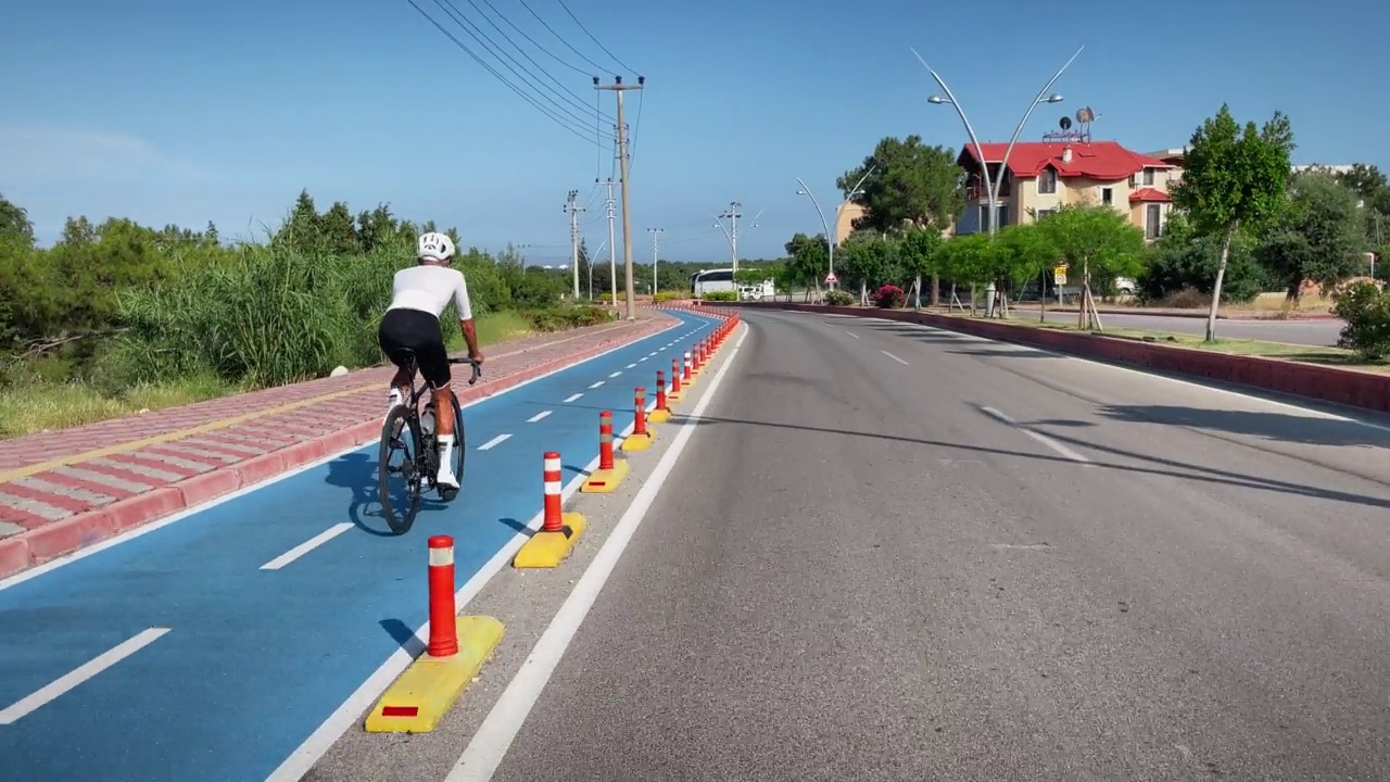 男自行车公路自行车。年轻的男自行车手骑在公路自行车外面。职业公路自行车手穿着自行车服，戴着白色头盔，在自行车道上骑自行车。运动动机。健身活动视频素材