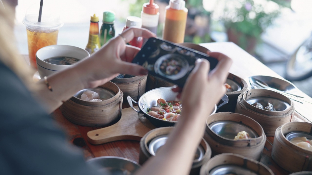 亚洲女人用手机拍桌子上的食物。视频素材