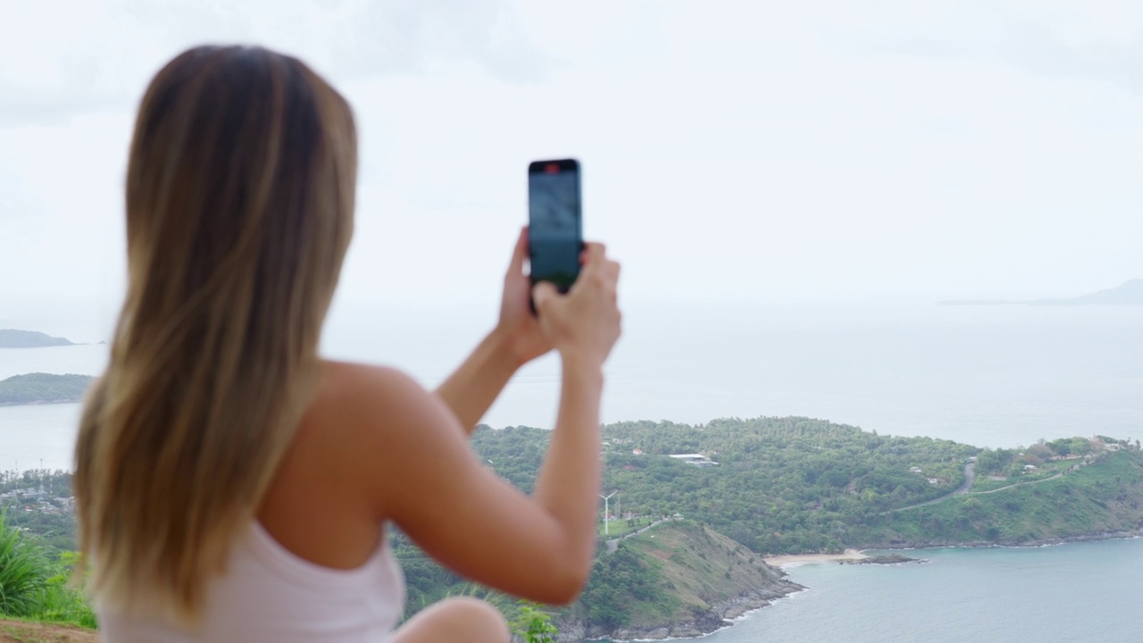 年轻的亚洲女子在热带岛屿旅行时用手机拍摄美丽的大海视频素材