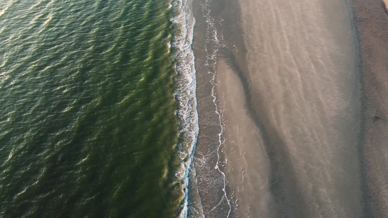 无人机从上空拍下的海岸，绿色的水飞溅在海滩上视频素材