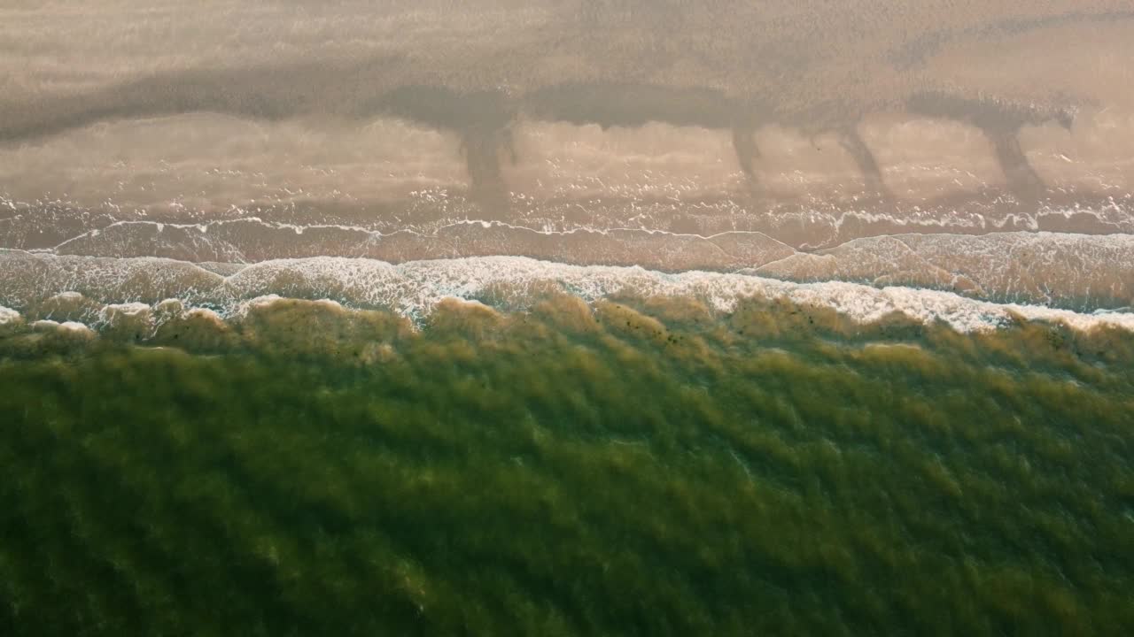 无人机从上空拍下的海岸，绿色的水飞溅在海滩上视频素材