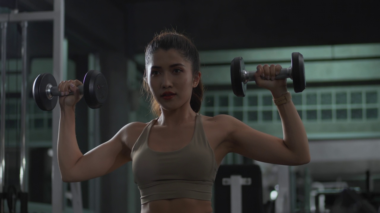 一位穿着内衣和紧身裤的年轻亚洲女性正在健身房举哑铃视频素材