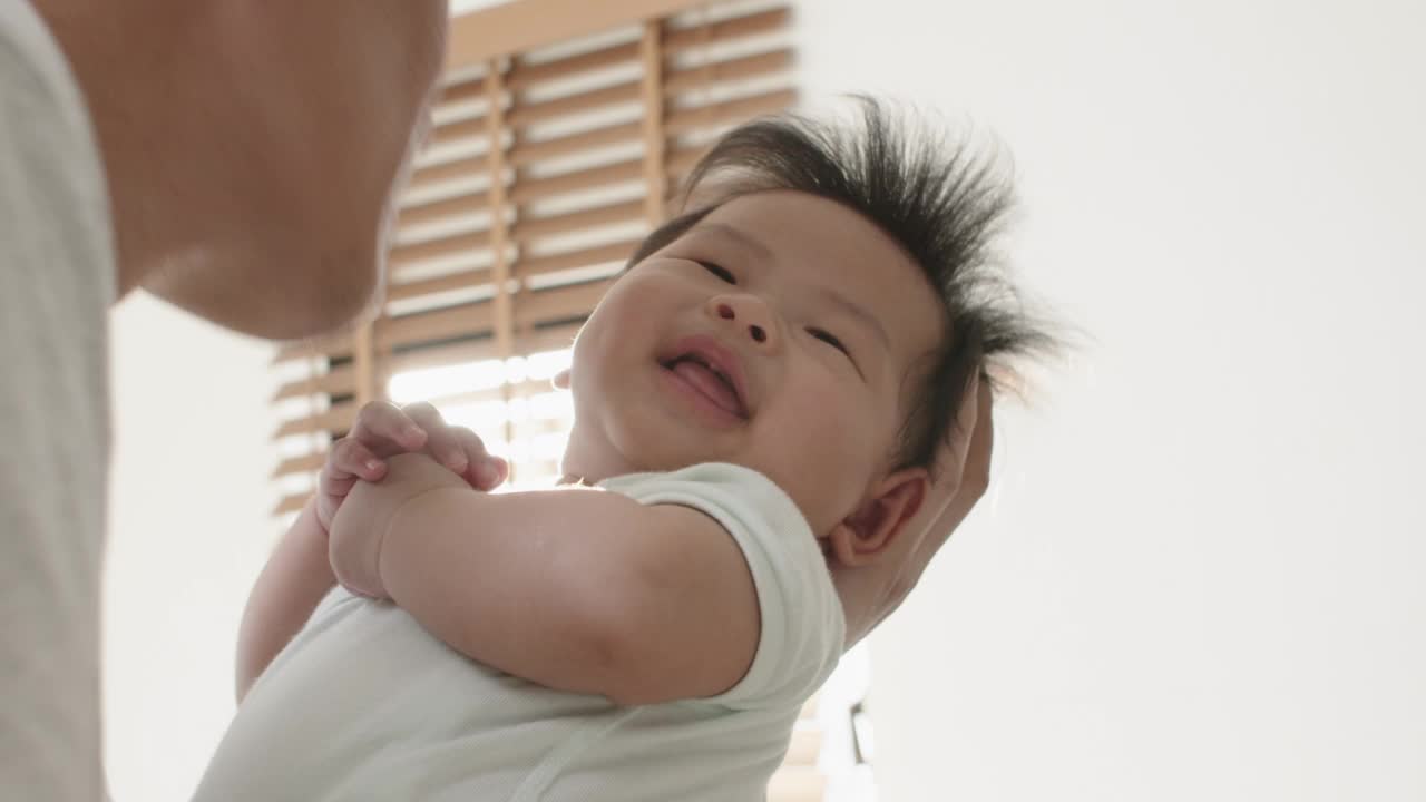 可爱的亚洲父亲在家里抱着并亲吻新生婴儿。视频素材