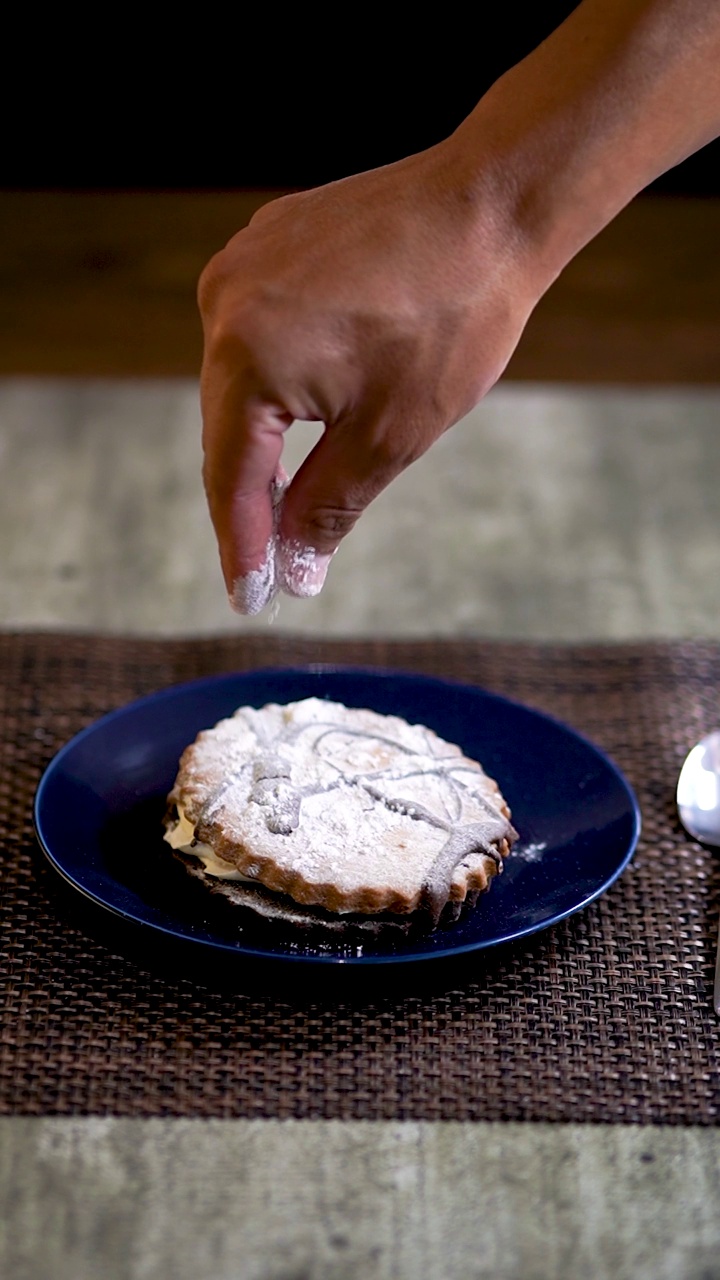 一个圆形饼干的垂直视频，填充polvoron，显示一只手在饼干上撒糖。视频素材