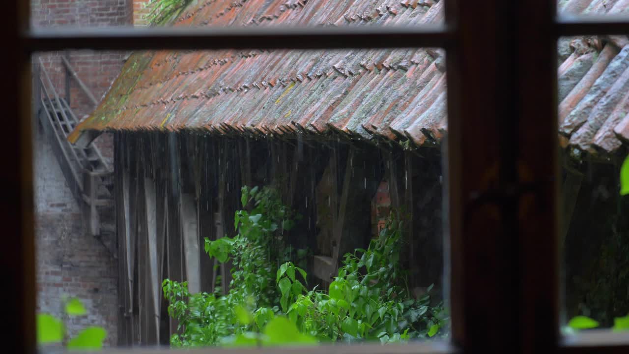 透过窗户看到雷雨中大雨打在老房子的屋顶瓦片上视频素材