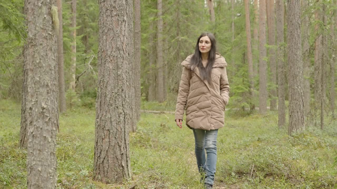 一个穿着牛仔裤和棕色夹克的女孩走过秋天的针叶林。前视图。视频素材