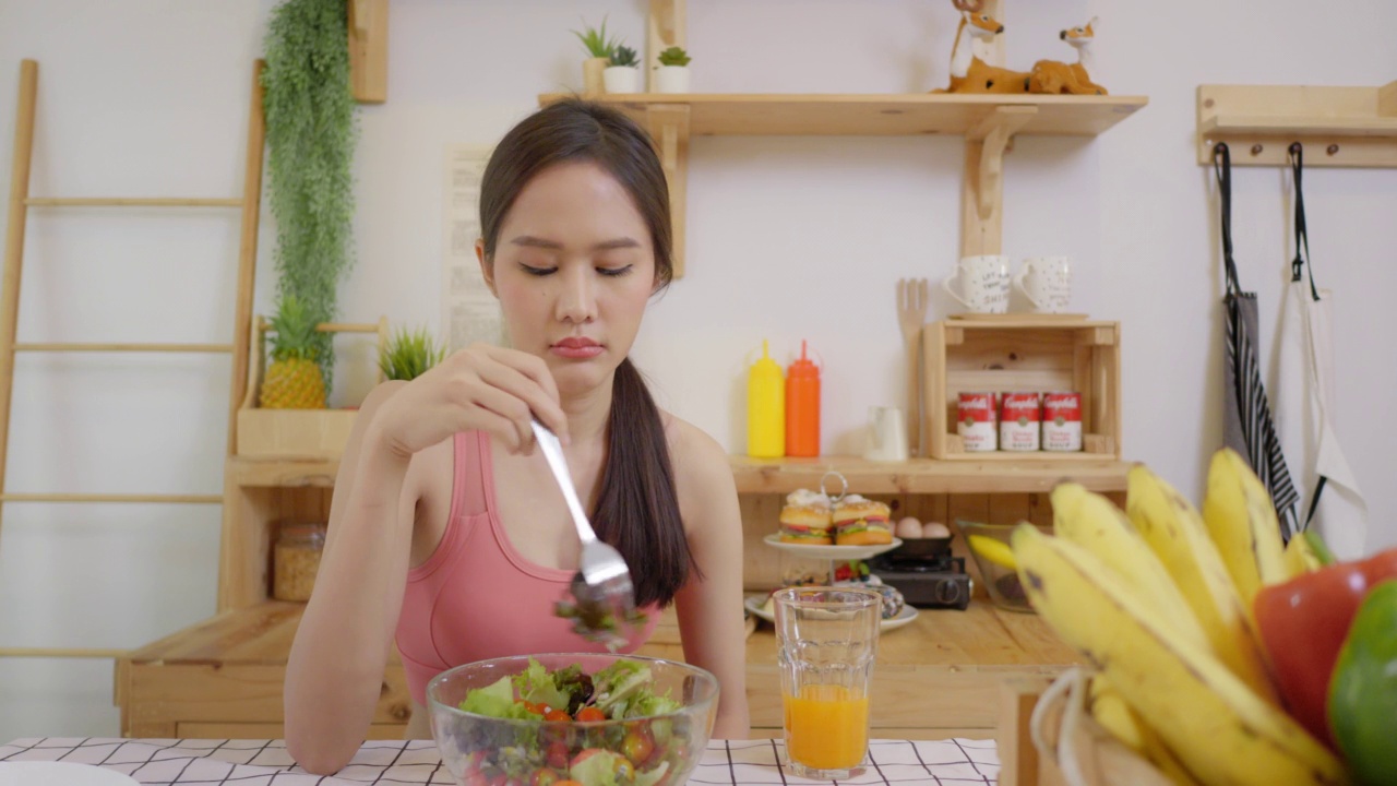 穿着运动服的亚洲女性不喜欢节食，吃蔬菜的时候表情呆滞。视频素材