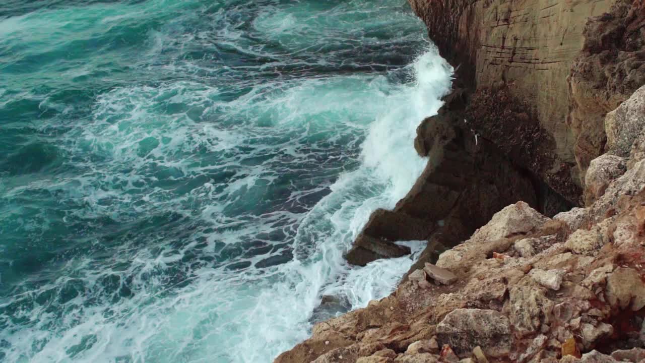 大海撞击岩石海岸，绿色的水飞溅和创造白色泡沫，从上面观看，慢动作视频视频素材