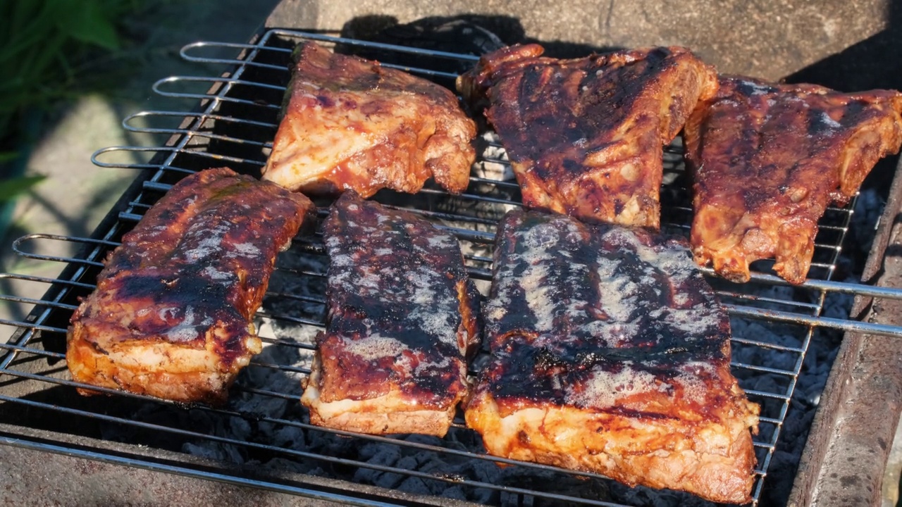 火焰烤架上的烤排骨。夏天的傍晚，人们在明火上烤排骨。美食户外午餐街头小吃慢动作特写视频素材