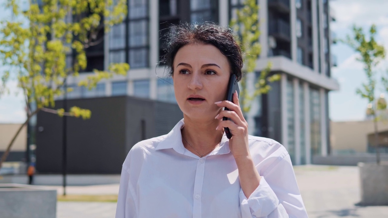 成功的黑发女商人在户外用手机讲话。女商人走在街上，用手机说话，接听商务电话。漂亮的女性专业交谈。视频素材